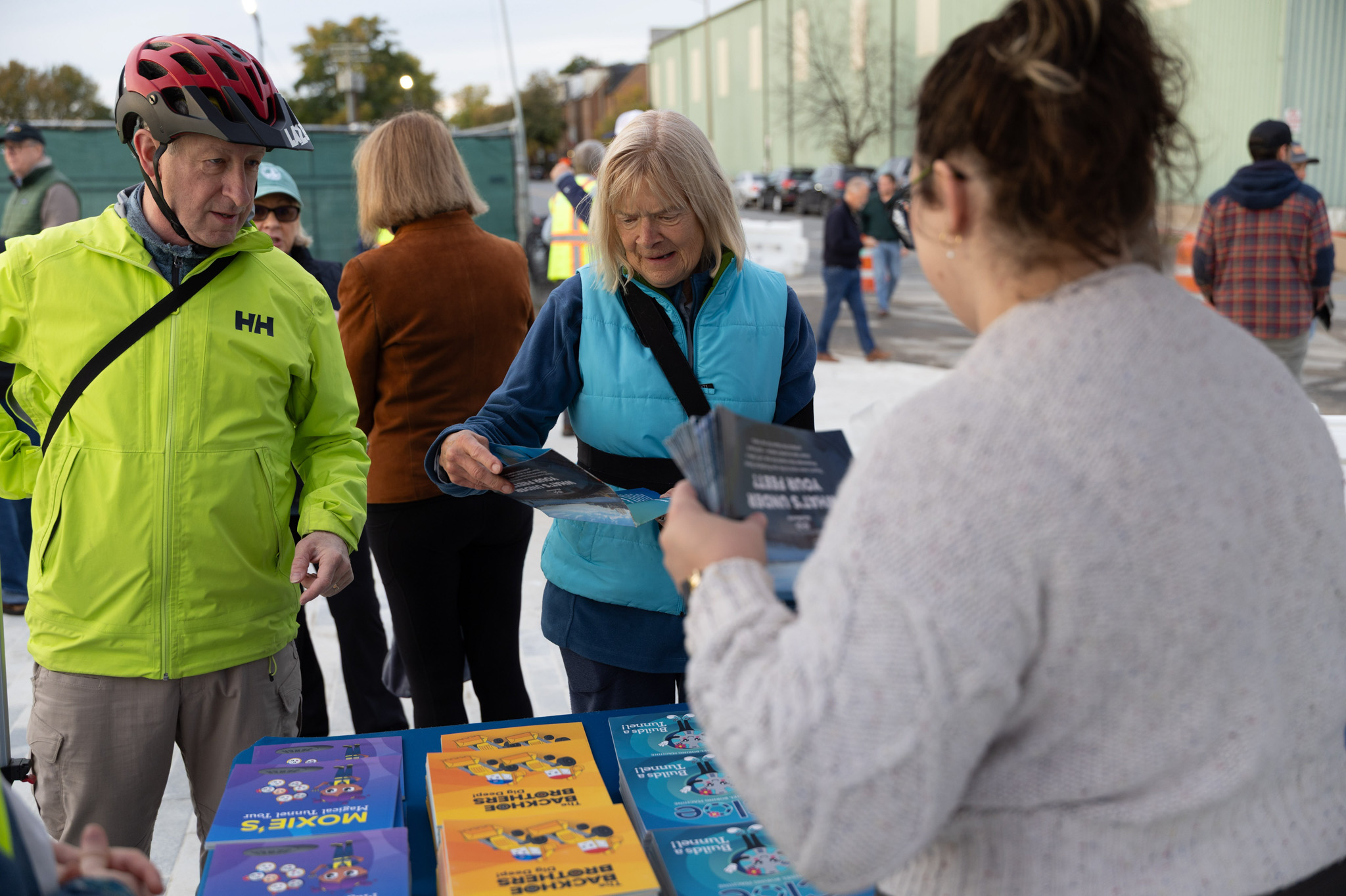 An elderly couple examine pamphlets at an AlexRenew informational table. An AlexRenew employee on the right side of the frame offers assistance.