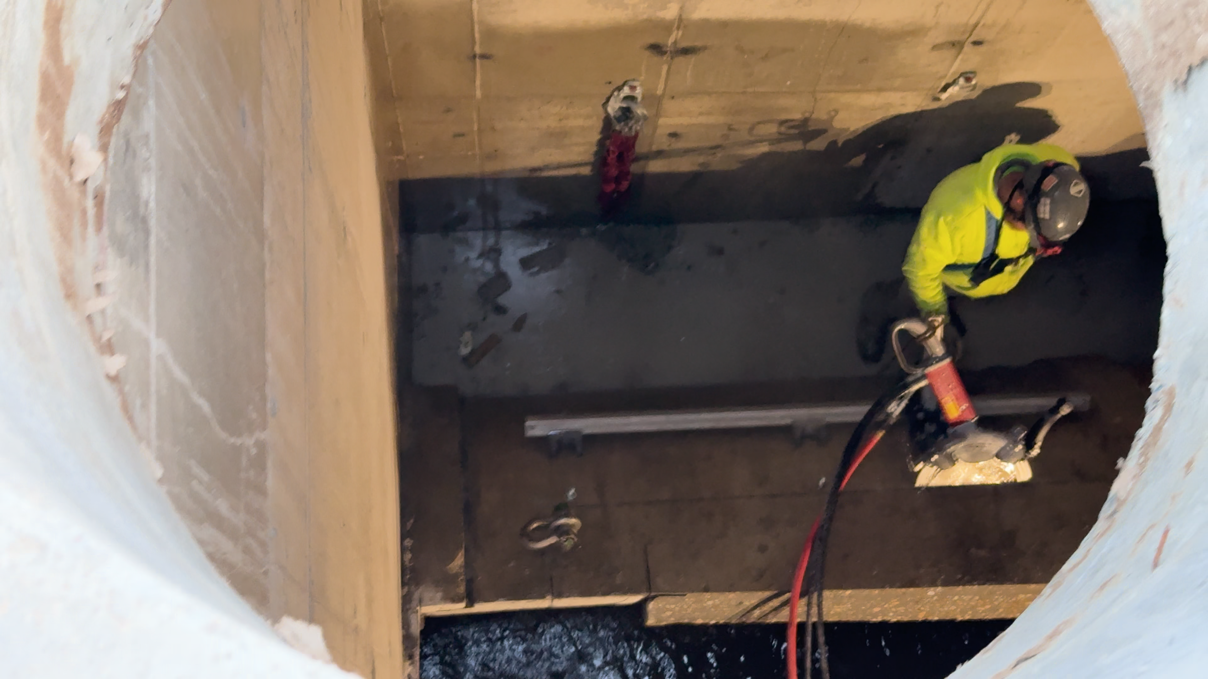 A man in high vis safety gear uses a saw to cut a concrete pipe. Water is visible inside the pipe in the lower left of the image.