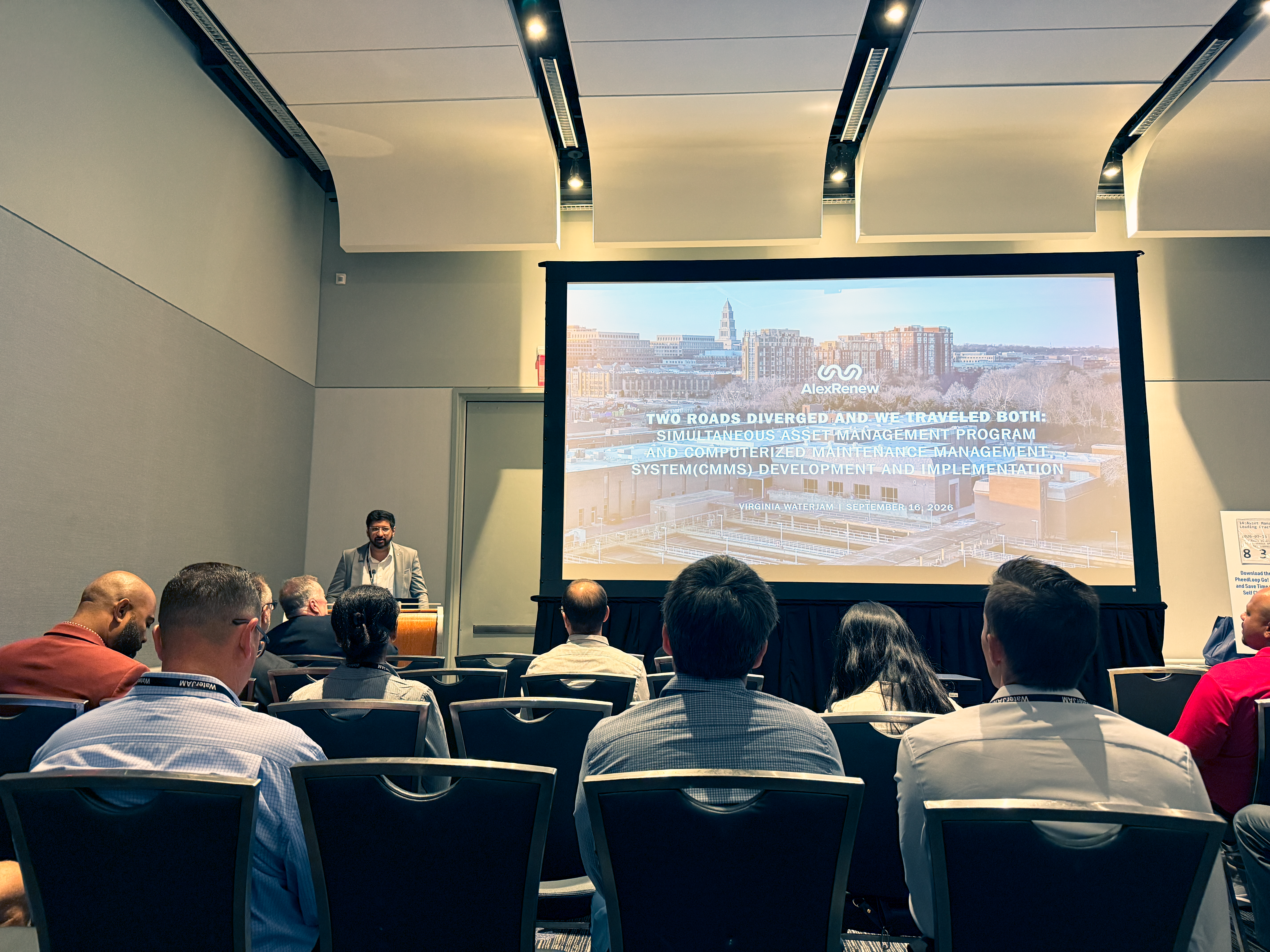 An AlexRenew employee speaks in front of a Powerpoint presentation to a conference room full of people.
