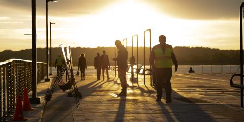 People silhouetted by the rising sun look at informational signs.
