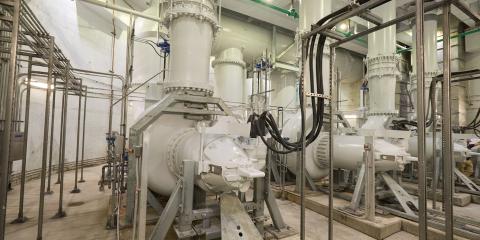 Large white pumps and pipes fill a high ceilinged room lit by florescent lights.
