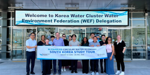 A group of people hold a banner beneath a sign that says "Welcome to Korea Water Cluster, Water Environment Federation (WEF)"