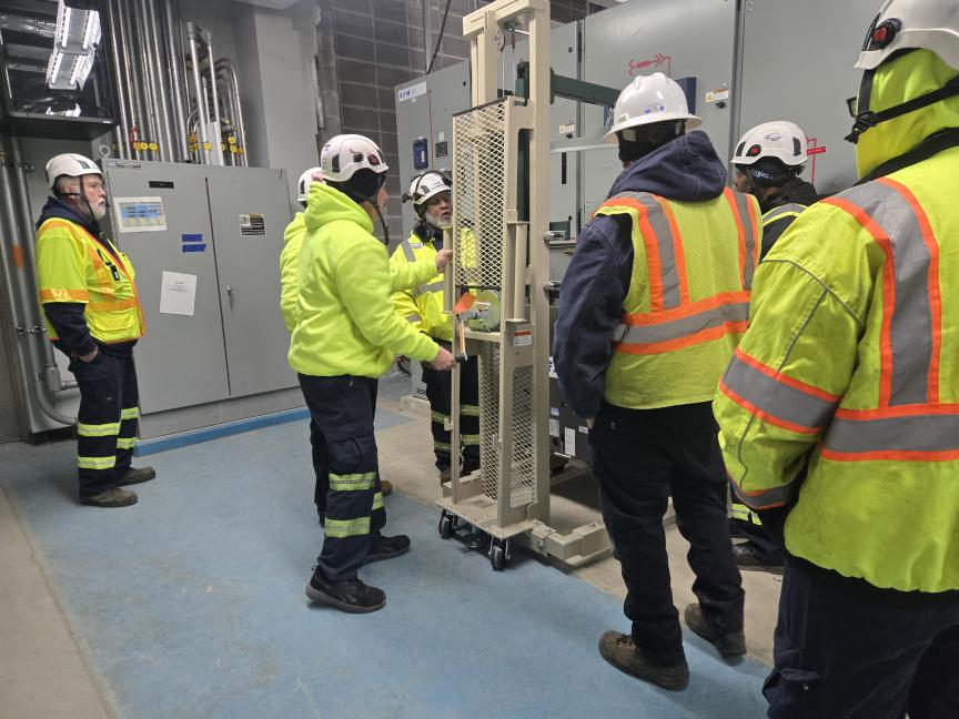 Wastewater plant operators in high vis jackets and hard hats gather around a piece of grey equipment.